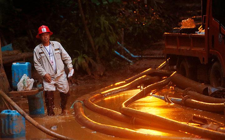 A rescuer makes his way down muddy steps past pump hoses at the entrance to a cave complex where 12 soccer team members and their coach went missing in Mae Sai, in northern Thailand.