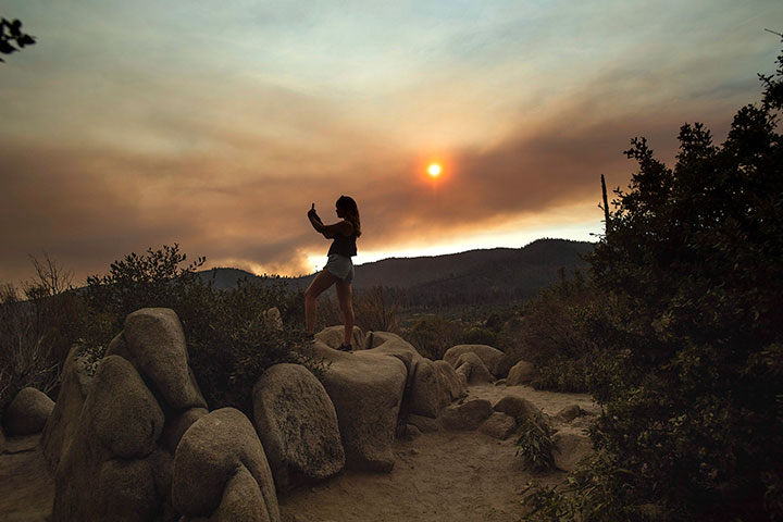 A woman photographs a plume of smoke from the Ferguson Fire in Yosemite National Park, Calif., on Tuesday, July 24, 2018.