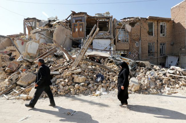 In this Nov. 16, 2017 file photo, Iranian people walk near a collapsed home in Kermanshah Province, Iran after an earthquake which killed at least 530 people. 