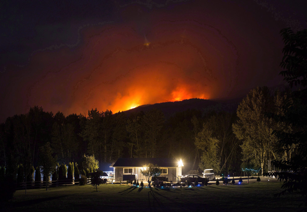  A wildfire burns on a mountain behind a home in Cache Creek, B.C., July 8, 2017. 