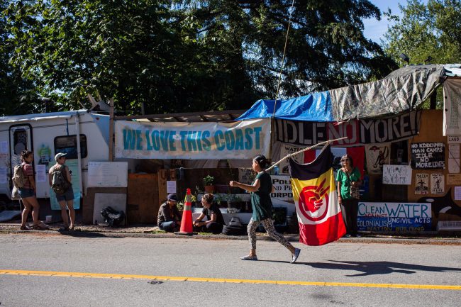 A woman walks with an American Indian Movement flag at Camp Cloud near the entrance of the Kinder Morgan Trans Mountain pipeline facility in Burnaby, B.C., July 21, 2018. 