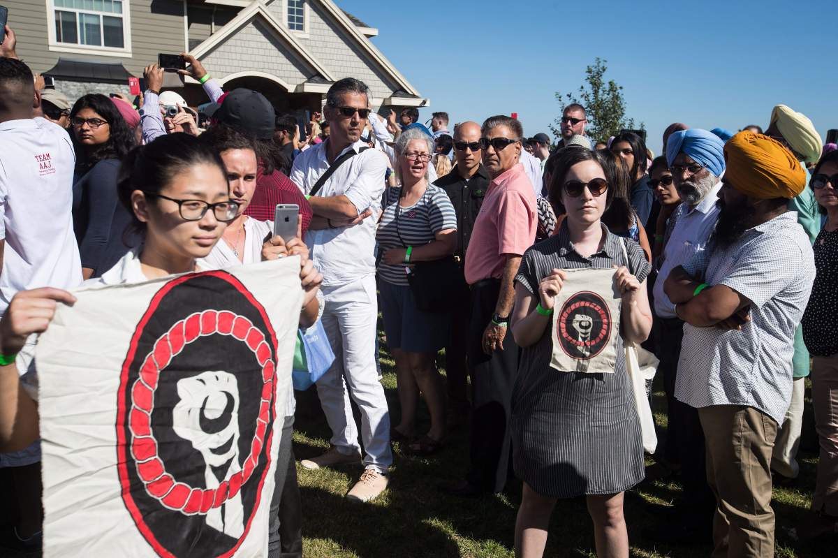 Protesters holding banners stand in the crowd as William George, a member of the Tsleil-Waututh First Nation and a guardian at the watch house near Kinder Morgan’s Burnaby facility, plays a drum and sings in protest as Prime Minister Justin Trudeau speaks at a Liberal Party barbecue in Delta, B.C., on Sunday August 5, 2018. (Darryl Dyck/The Canadian Press)