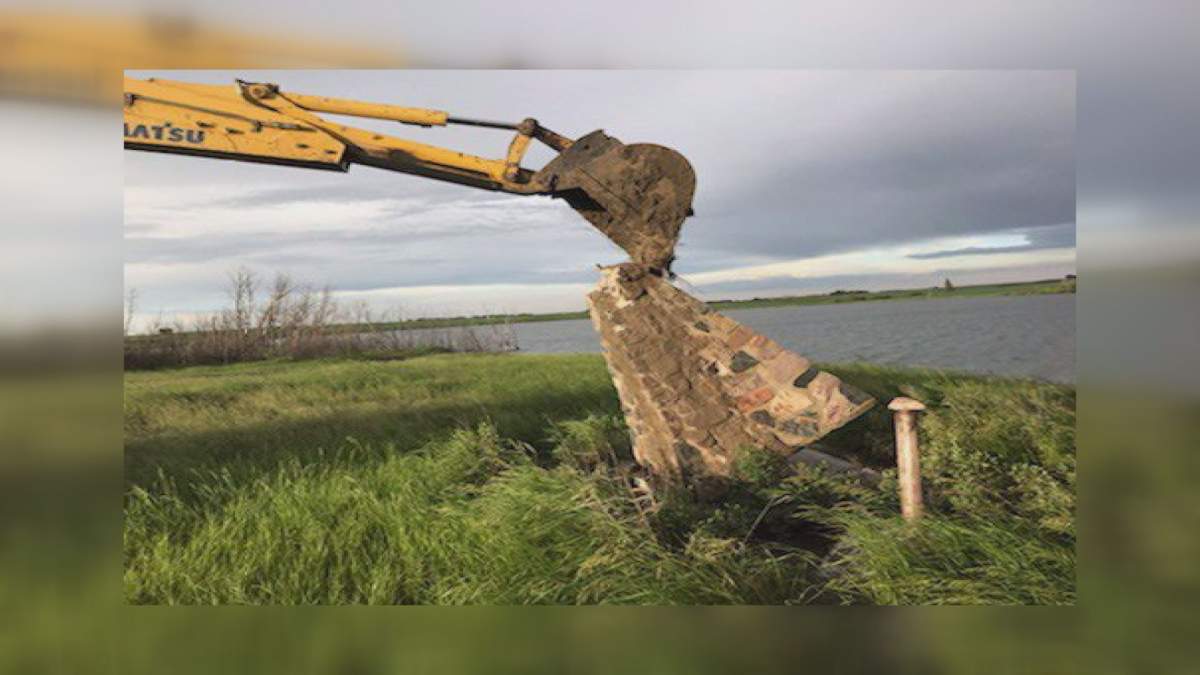 A backhoe tilts a cairn that contains a timecapsule in this handout image. When a Saskatchewan village held a summer party to crack open a time capsule sealed in a cairn 50 years ago, they expected it would contain centennial coins, newspapers, letters from the children at the community's former school and mementos of rural Canadian life in the 1960s. 