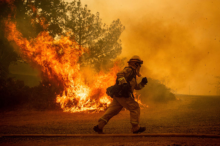A firefighter runs while trying to save a home as a wildfire tears through Lakeport, Calif., Tuesday, July 31, 2018.