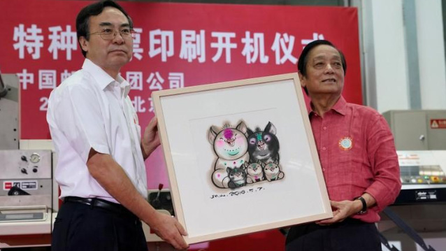 Designer Han Meilin, right, poses for pictures as he presents his design manuscript for a Year of the Pig stamp to Liu Aili, president of China Post, at a ceremony in Beijing, China on Aug. 6, 2018.