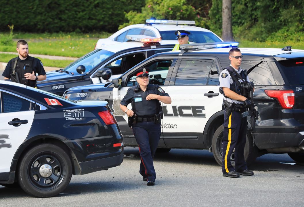 Police and RCMP officers survey the area of a shooting in Fredericton, N.B., on Aug. 10, 2018.
