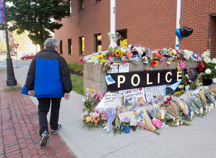 A resident views the makeshift tribute outside the police station in Fredericton on Saturday, Aug. 11, 2018. Two city police officers were among four people who died in a shooting in a residential area on the city's north side.