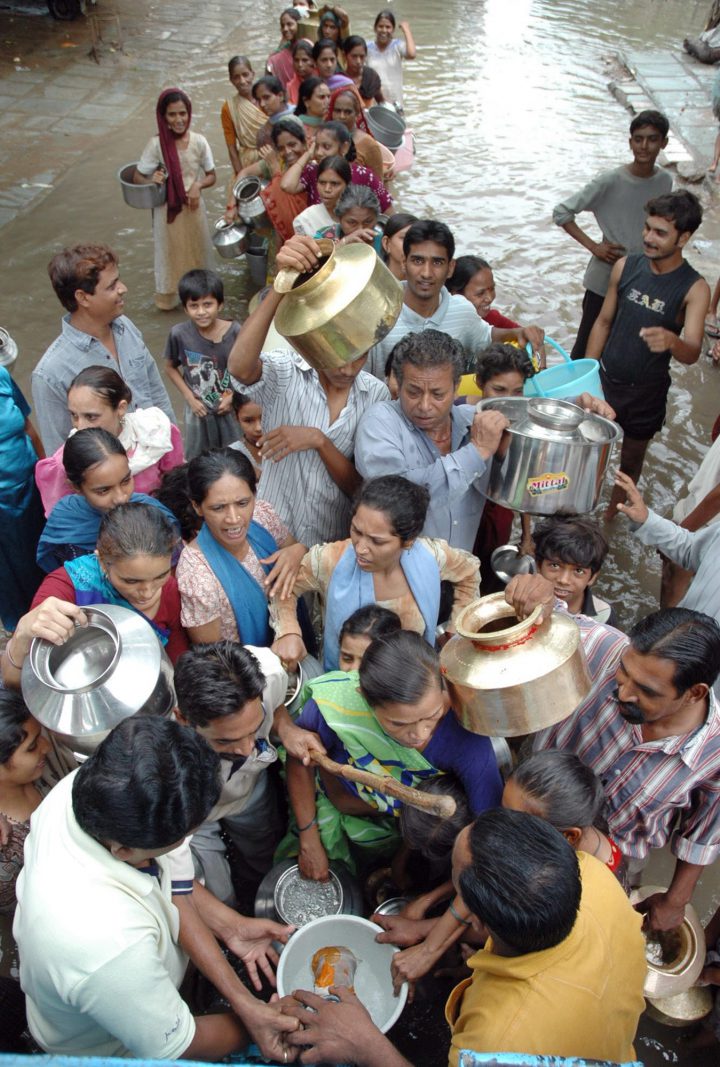 People stand in floodwaters to collect drinking water distributed by authorities in Baroda, about 115 kilometers (72 miles) south of Ahmadabad, India, Monday, July 4, 2005.