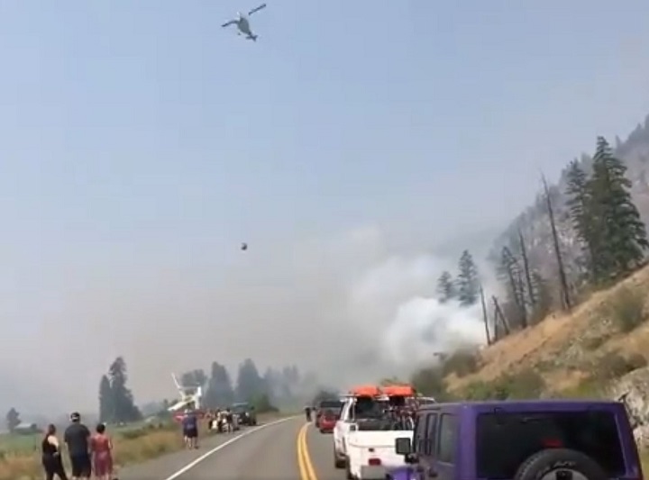 This still from a video clip shows a helicopter bucketing water on a fire alongside Highway 3 near Hedley, B.C.
