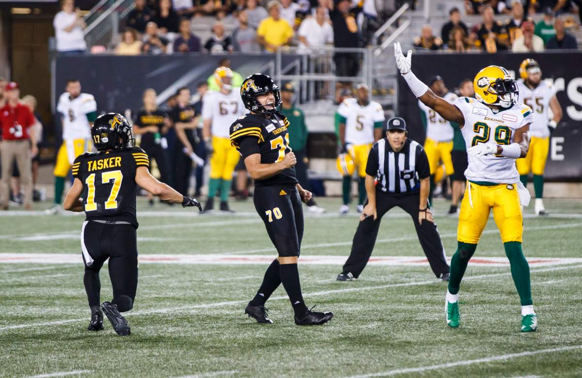 Hamilton Tiger-Cats kicker Lirim Hajrullahu celebrates kicking the winning field goal with teammate Luke Tasker, left, against Edmonton Eskimos' Mercy Maston, right, during the second half of CFL football action in Hamilton, Ontario on Thursday August 23, 2018.