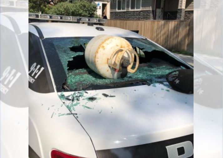 A man was arrested after throwing a propane tank through the rear window of a police car for no apparent reason.