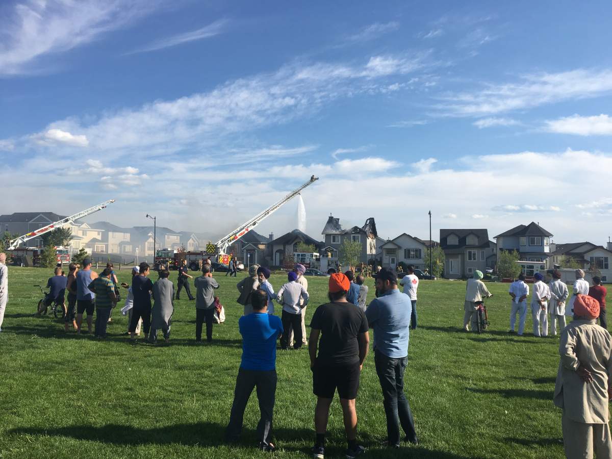 People watch as fire crews battle a blaze at three homes in northeast Calgary on Monday, Aug. 6.