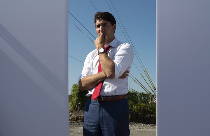 Prime Minister Justin Trudeau listens to a presentation between two signs, before participating in a ground-breaking ceremony for a distribution centre in Ottawa, Monday Aug. 20, 2018.