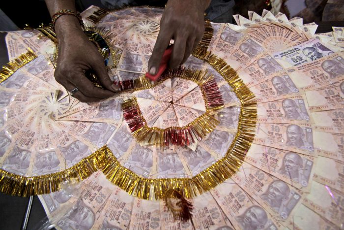 In this Nov. 11, 2016 file photo, a shopkeeper prepares a garland with Indian 10 Rupees denomination notes, used particularly to garland grooms on their wedding day, in Jammu, India. 