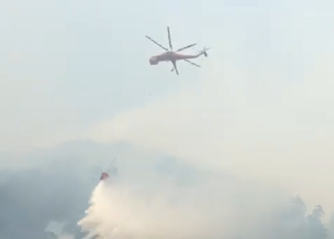 A helicopter dumps water on a wildfire burning next to the small coastal community of Zeballos, B.C.