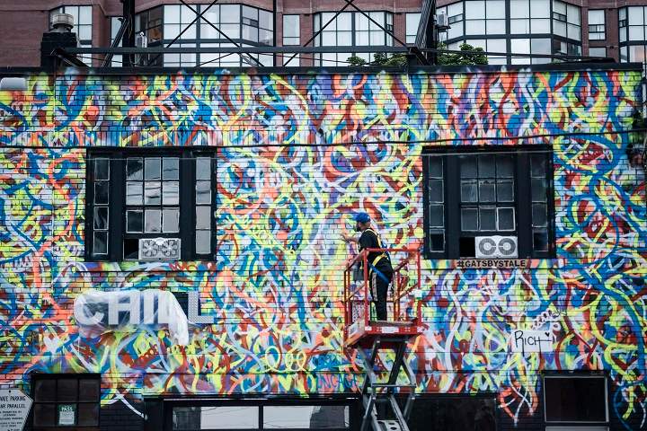 Anthony Ricciardi spray paints the eastern facade of a commercial establishment on Bathurst Street in Toronto, on Monday, July 30, 2018. 