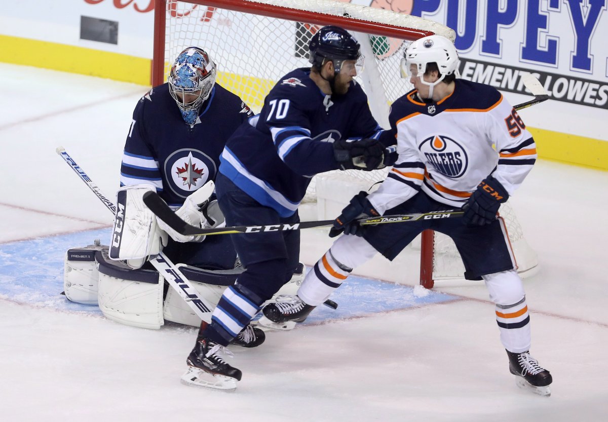 Edmonton Oilers' Kailer Yamamoto (56) tips a shot past Winnipeg Jets' goaltender Connor Hellebuyck (37) as he's checked by Joe Morrow (70) during first period preseason NHL hockey action in Winnipeg, Sunday, September 23, 2018. THE CANADIAN PRESS/Trevor Hagan.