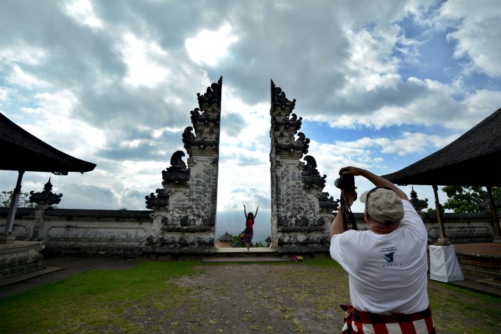 Tourists take photos by an arch on the Lempuyang Temple grounds as Mount Agung volcano is seen obscured by clouds in the background in Karangasem on Bali island on Oct. 4, 2017.