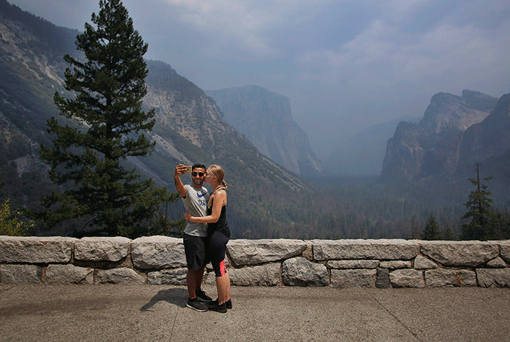 A couple takes a selfie in front of the famed Tunnel View vista in Yosemite National Park as smoke is seen from existing wildfires in the area, Tuesday, Aug. 14, 2018 in Calif. 