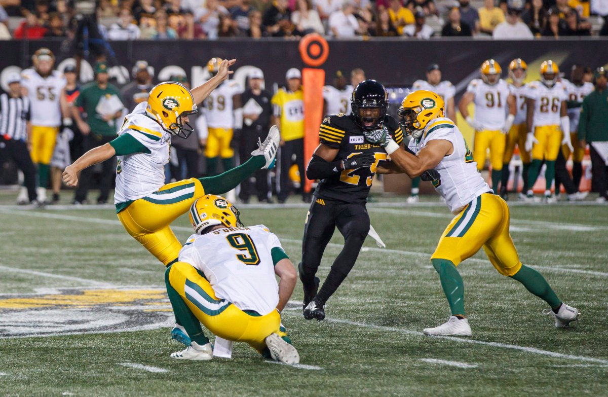 Edmonton Eskimos' Sean Whyte, left, kicks a 52 yard field goal as teammates Danny O'Brien, second left, and Korey Jones, right, defend against Hamilton Tiger-Cats' Jumale Rolle during the first half of CFL football action in Hamilton, Ontario on Thursday August 23, 2018. 