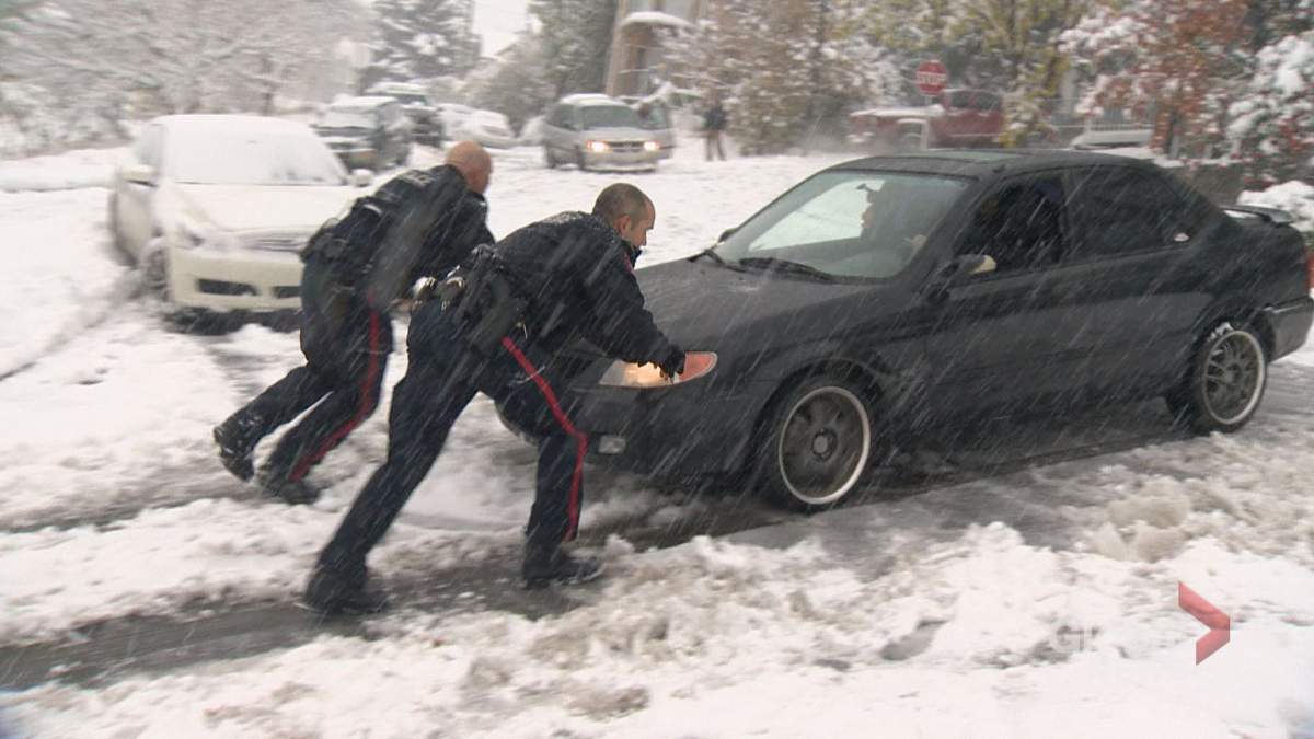 Calgary police officers help push out a vehicle stuck in the snow as fall storm hits the city Tuesday, Oct. 2, 2018.