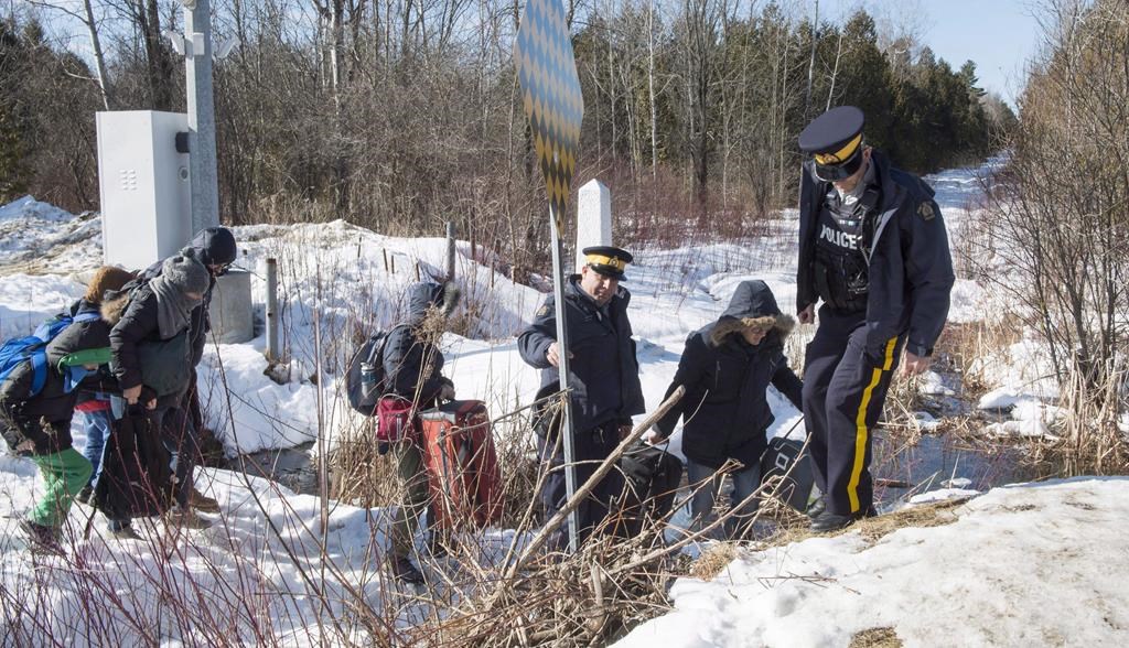 RCMP officers help a family of asylum claimants as they cross the border into Canada from the United States, Monday, February 20, 2017 near Hemmingford, Que. THE CANADIAN PRESS/Paul Chiasson.