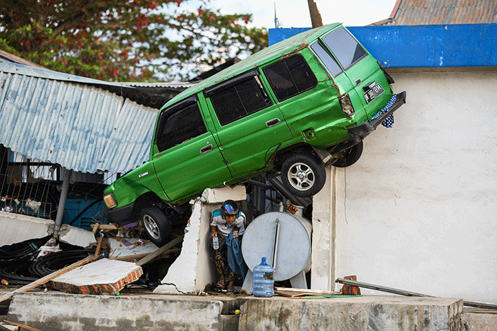 A survivor walks under a car struck on a building in Palu, Indonesia’s Central Sulawesi on October 1, 2018.
