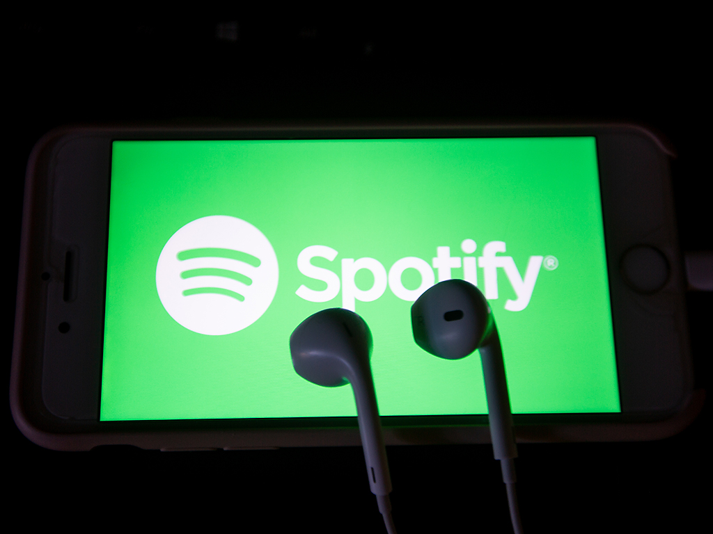Music streaming app Spotify is seen on a screen with some headphones lying on it.