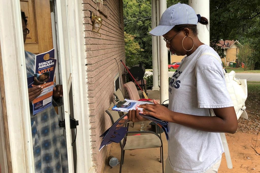 FILE - In this Monday Oct. 8, 2018, photo, Leila Hart, 21, explains early voting and absentee voting to a resident in Forest Park, Ga.