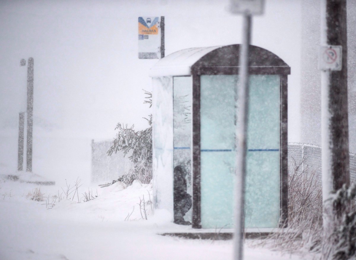 A person hides from the snow in a bus shelter in Halifax on Tuesday, March 13, 2018.