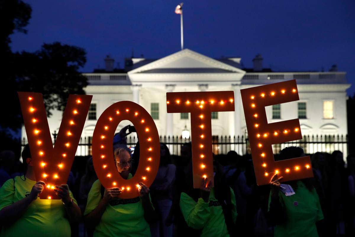 FILE - In this Oct. 6, 2018 file photo, Nancy McCullough, of Reston, Va., looks out the center of a letter "o" as she and other members of the group, Herndon Reston Indivisible, hold up letters spelling "vote them out" during a protest of the confirmation of Brett Kavanaugh to the Supreme Court outside of the White House in Washington. Brett Kavanaugh's confirmation is a flashpoint for the November midterms.  (AP Photo/Jacquelyn Martin, File).