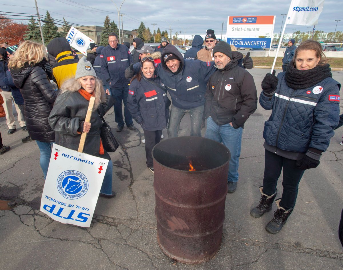 Striking Canada Post workers stay warm around the fire as they walk the picket line  in Montreal on Tuesday, Oct. 30. Workers in Hamilton, Regina and La Mauricie, Que., have also joined the rotating strikes.
