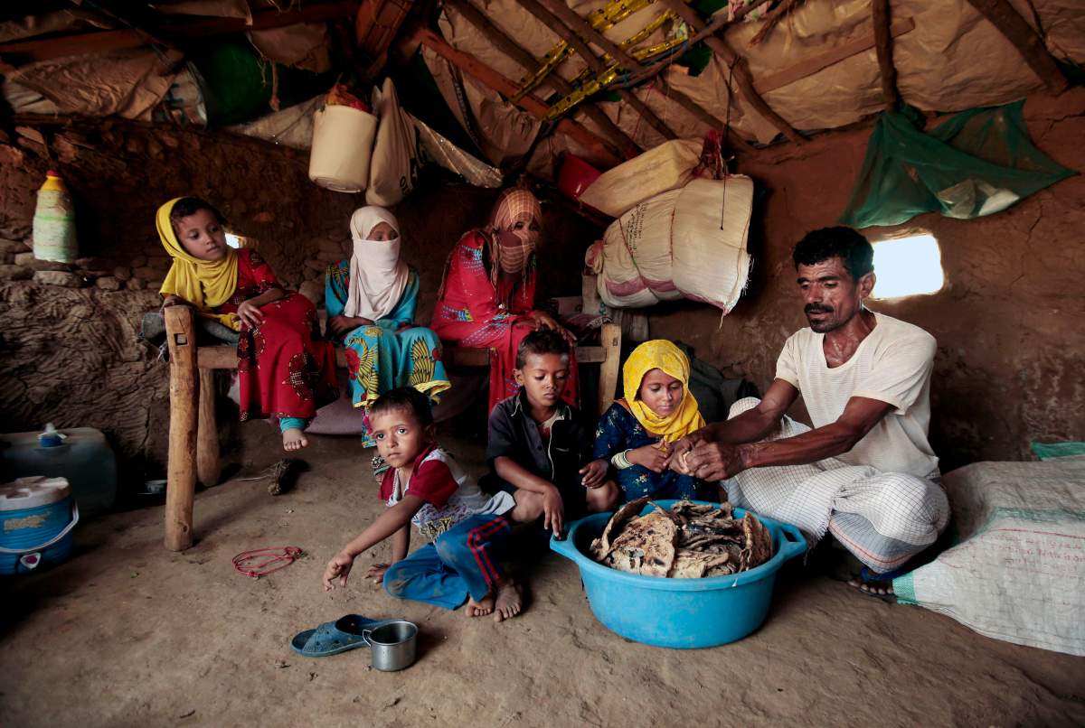 In this Oct. 1, 2018, photo, Yahia Hussein feeds his children mouldy bread in their shelter, in Aslam, Hajjah, Yemen. 