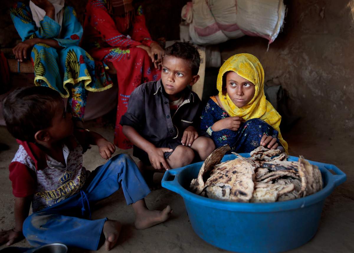 In this Oct. 1, 2018, photo, children sit in front of mouldy bread in their shelter, in Aslam, Hajjah, Yemen. In a plastic washtub, the children’s mother collects hard bread crumbs even those covered with mold, then mix with water, add salt, and give to her four children.