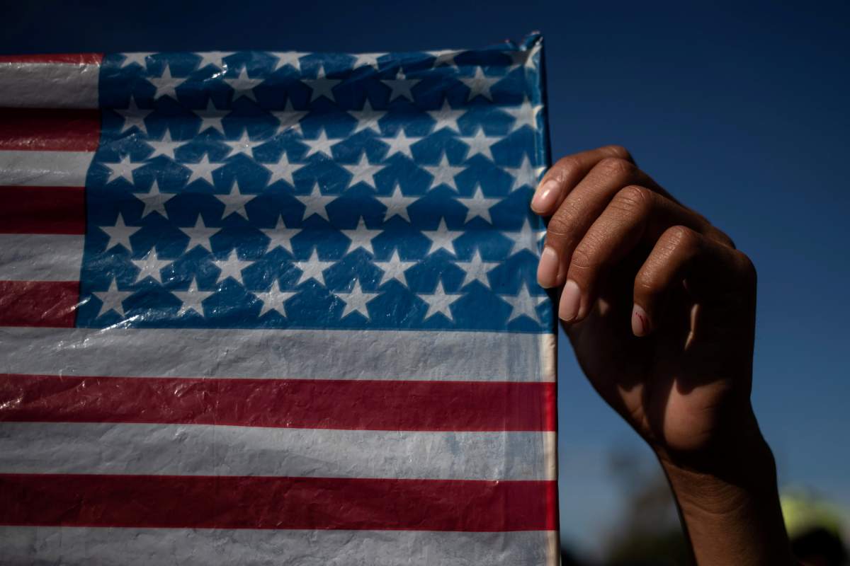 A migrant, part of a caravan of thousands from Central America, raises the U.S. flag as he takes part in a march to the United States border in Tijuana, Mexico, Nov. 25, 2018.