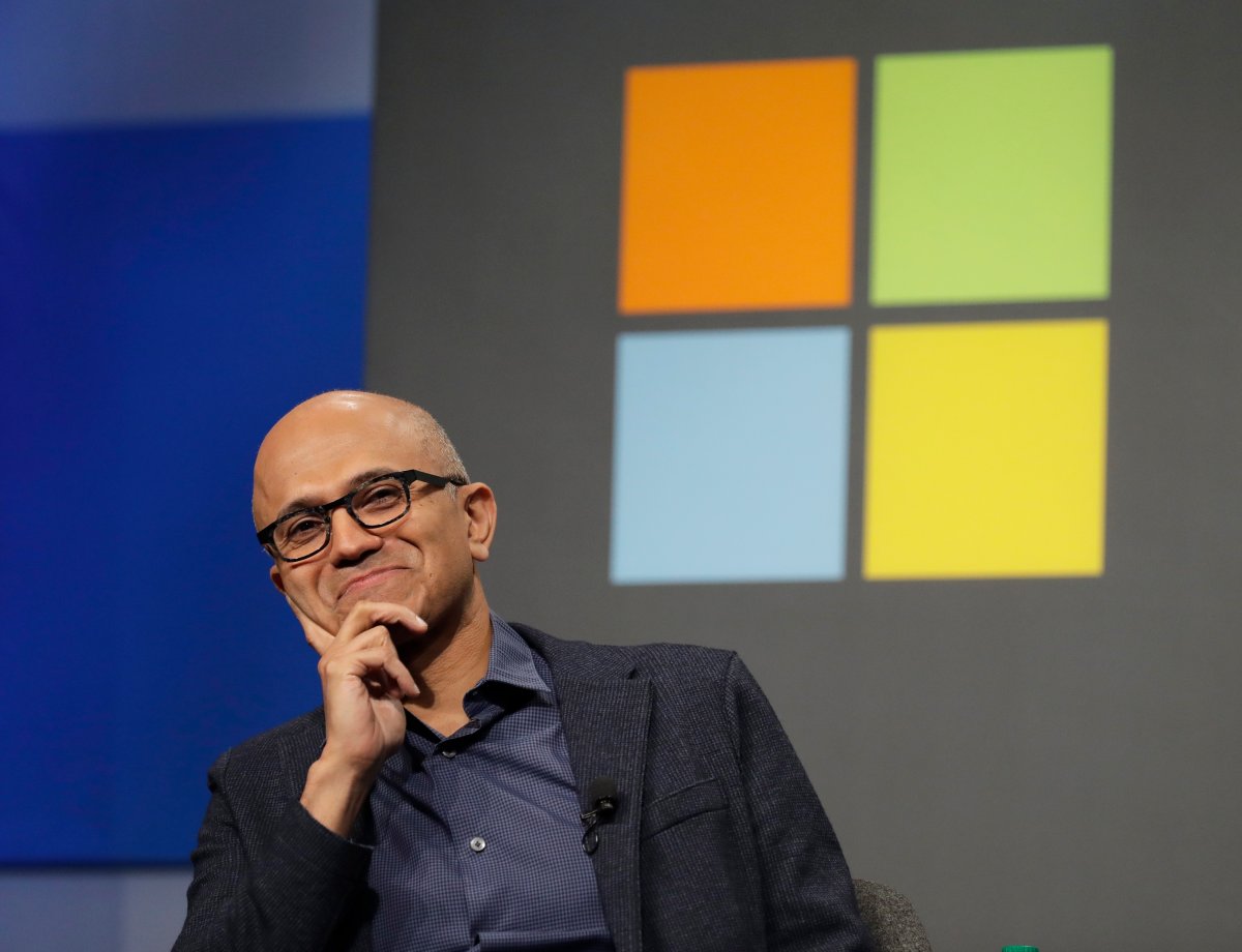 FILE- In this Wednesday, Nov. 28, 2018, file photo Microsoft CEO Satya Nadella listens to a question as he sits in front of the Windows logo during the annual Microsoft Corp. shareholders meeting in Bellevue, Wash.
