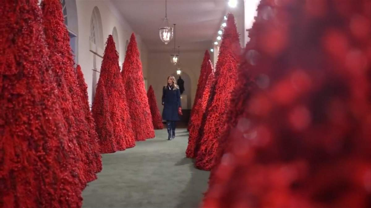First Lady Melania Trump passes a hall of red Christmas trees at the White House in 2018.