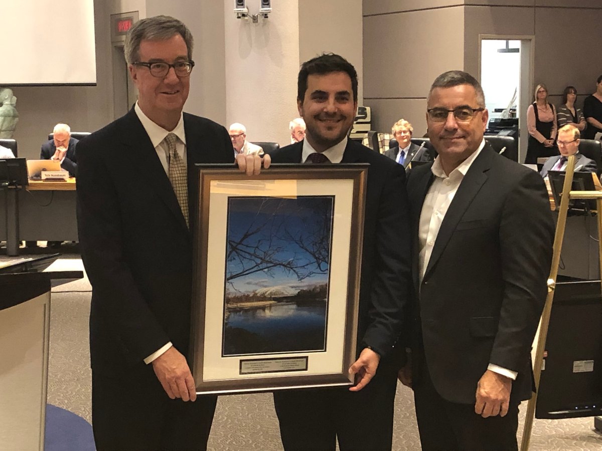 Coun. Michael Qaqish (centre) accepts a photo of the Chapman Mills Conservation Area as a farewell gift from Mayor Jim Watson and city manager Steve Kanellakos at a ceremony before council on Wednesday.