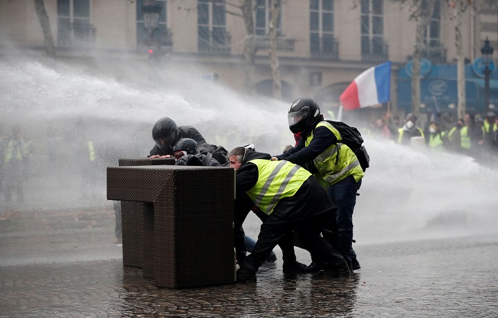 Protesters wearing yellow vests, a symbol of a French drivers’ protest against higher fuel prices, stand up in front of a police water canon during clashes on the Champs-Elysees in Paris, France, November 24, 2018.