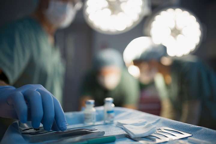 Surgeon reaching for instrument on tray operating room. 