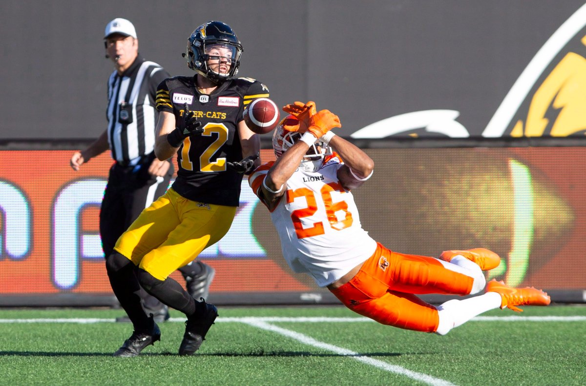 The ball slips through the hands of B.C. Lions defensive back Anthony Orange (26) straight into the hands of Hamilton Tiger-Cats wide receiver Mike Jones (12) during first-half CFL game action in Hamilton, Ont., on Saturday, Sept. 29, 2018.