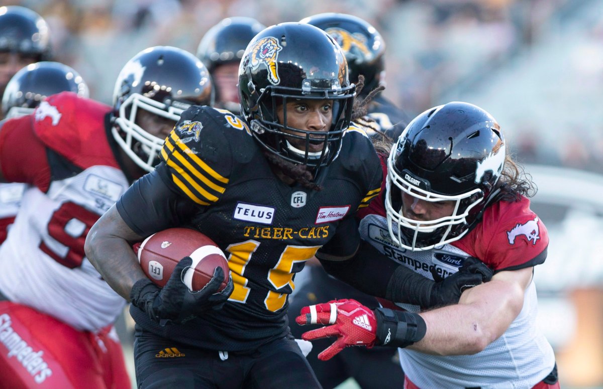 Hamilton Tiger-Cats running back Alex Green (15) tries to fend off defender Calgary Stampeders line backer Alex Singleton (49) during second half CFL football game action in Hamilton, Ont., on Saturday, Sept. 15, 2018.