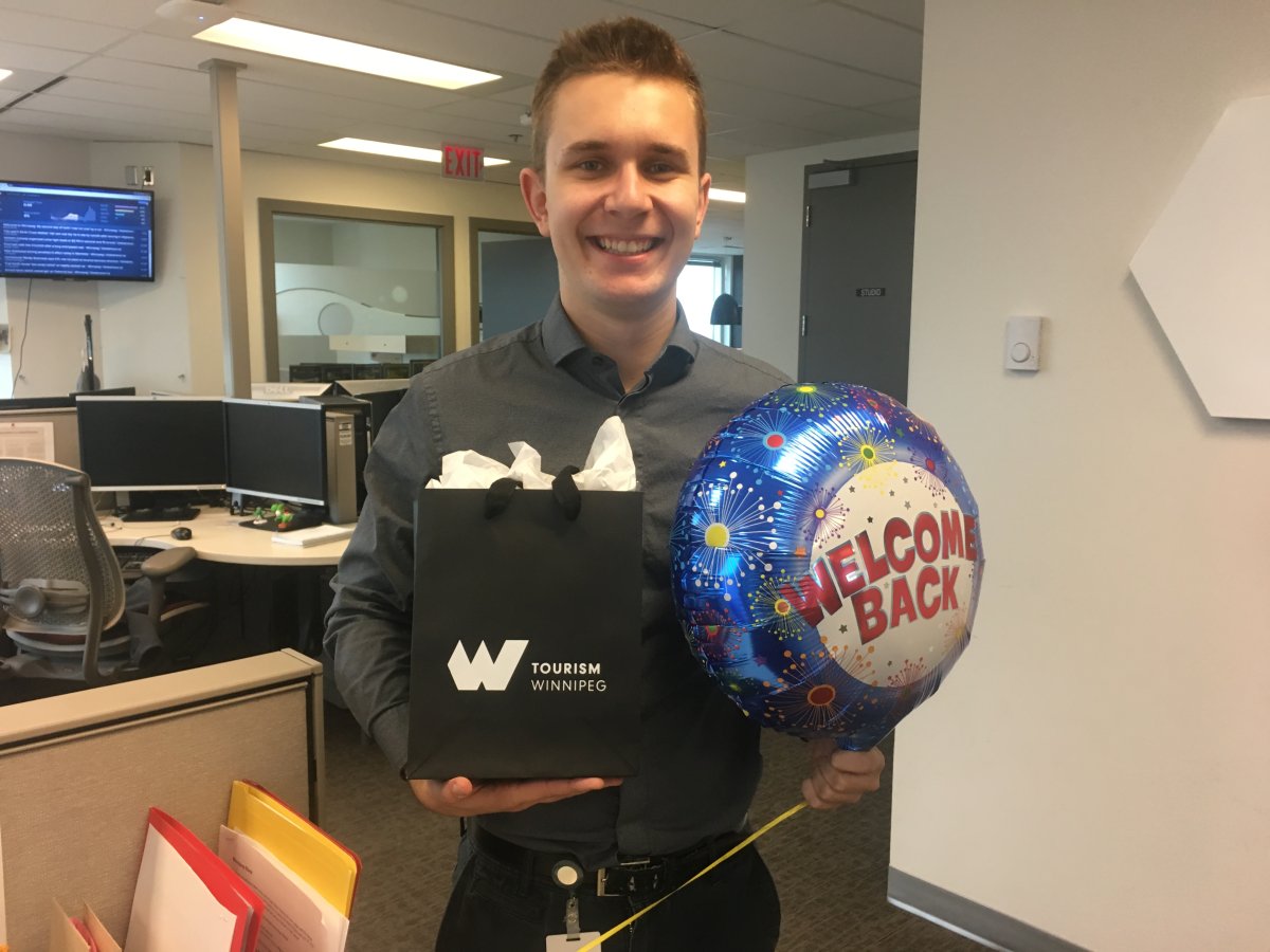 Myself standing beside my desk with welcome back gifts courtesy of Tourism Winnipeg, and my co workers.