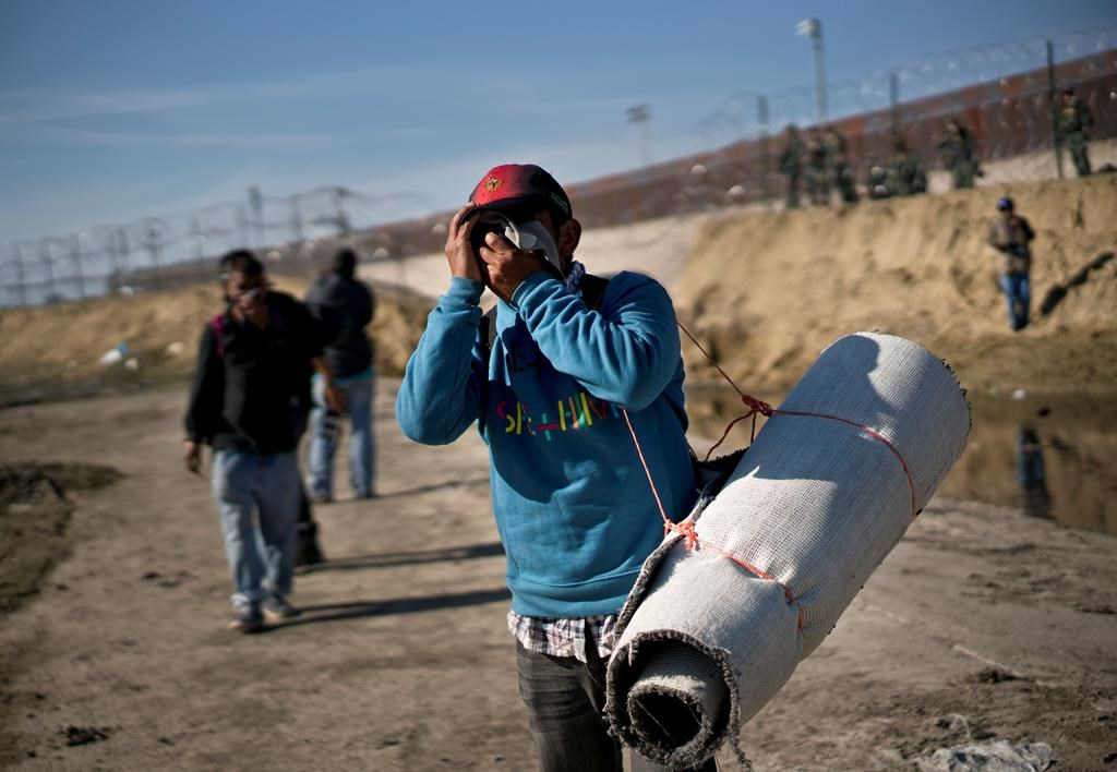 A migrant carrying a roll of carpet wipes his face after U.S. border agents fired tear gas at a group of migrants who had pushed past Mexican police at the Chaparral border crossing in Tijuana, Mexico, Sunday, Nov. 25, 2018.