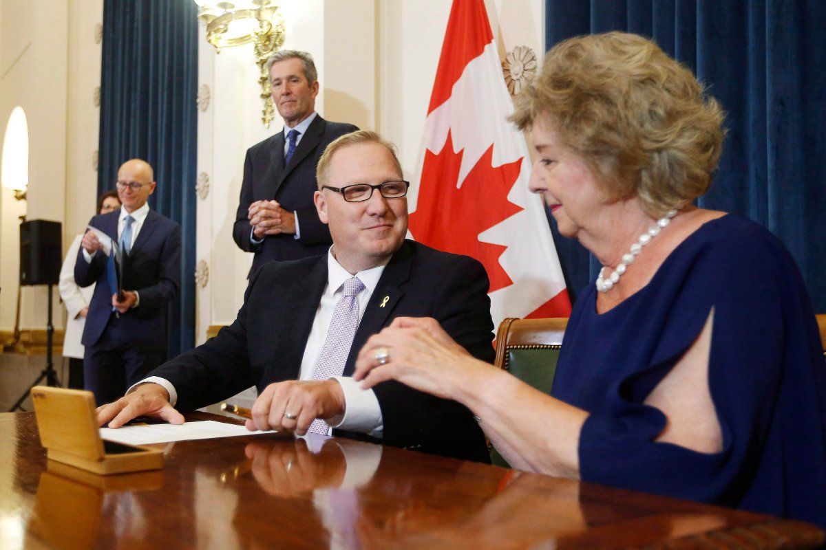 Scott Fielding, MLA for Kirkfield Park, centre signs documents with Lieutenant Governor Janice Filmon after he is sworn into cabinet as the new minister of Finance and minister responsible for the civil service during Premier Brian Pallister's cabinet shuffle announced at the Manitoba Legislature in Winnipeg on Wednesday, August 1, 2018. 