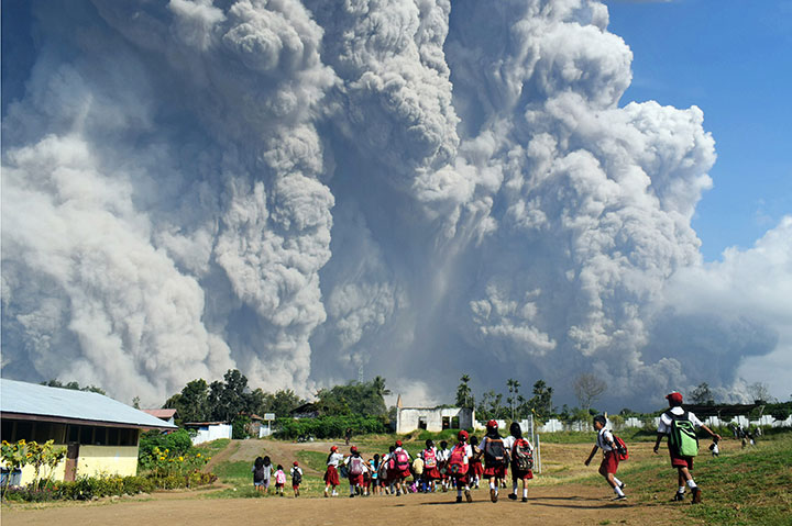 Indonesian schoolchildren walk together in Tiga Pancur village, North Sumatra on February 19, 2018, as thick volcanic ash from Mount Sinabung volcano rises into the air.