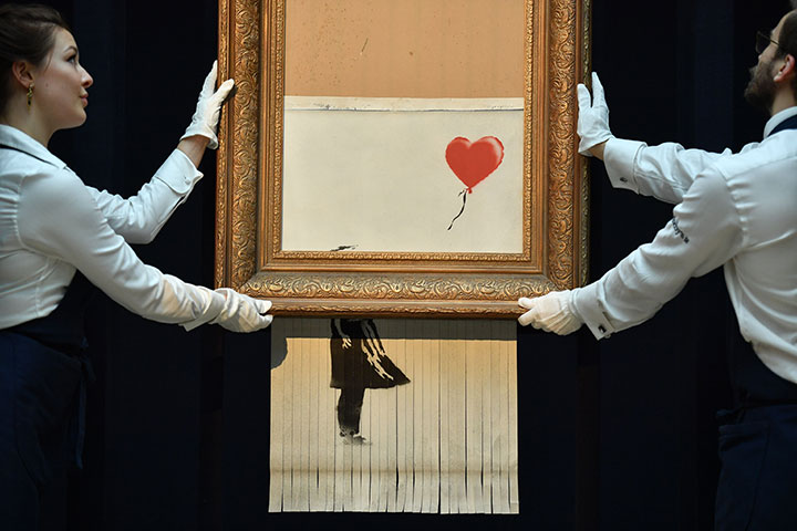 Sotheby’s employees pose with the newly completed work by artist Banksy entitled “Love is in the Bin”, a work that was created when the painting “Girl with Balloon” was passed through a shredder in a surprise intervention by the artist, at Sotheby’s auction house in London on October 12, 2018.