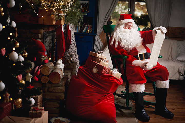 Santa Claus pictured sitting in chair with sack full of presents, looking at a list, probably checking it twice. 