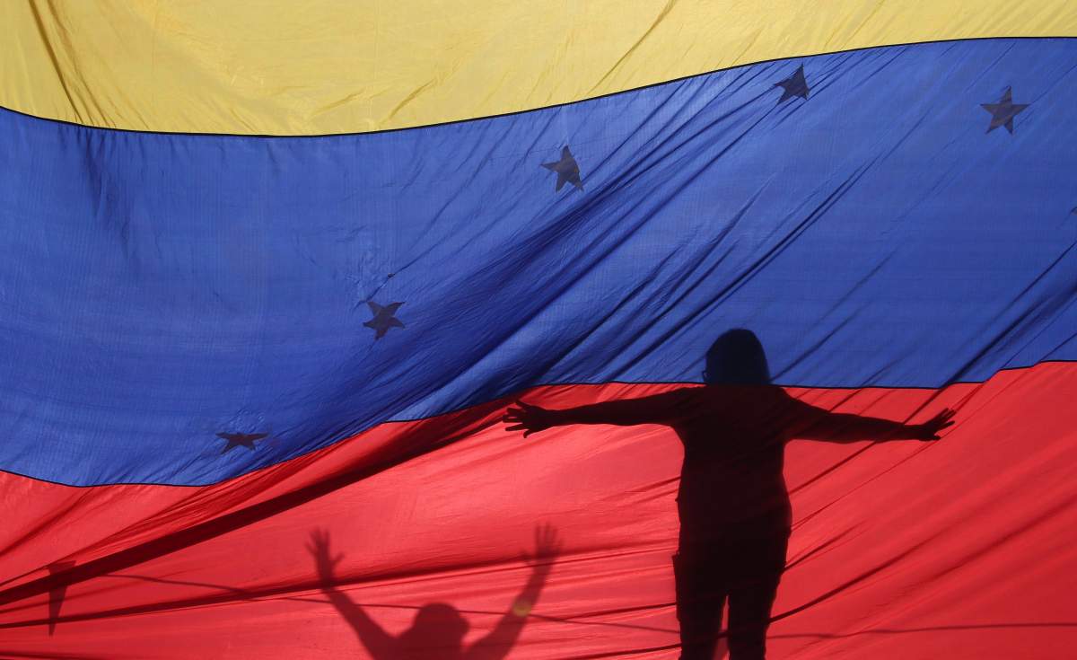 In this July 10, 2017 file photo, the silhouettes of anti-government protesters are seen through a Venezuelan flag.