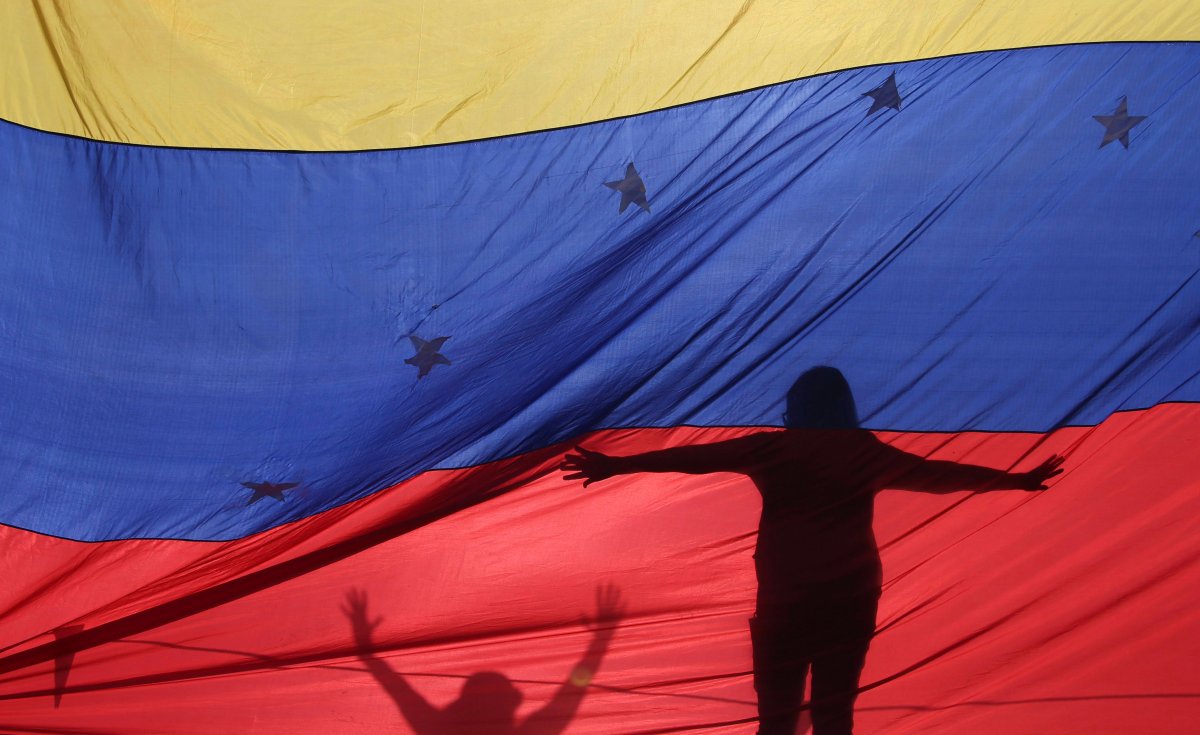 In this July 10, 2017 file photo, the silhouettes of anti-government protesters are seen through a Venezuelan flag.